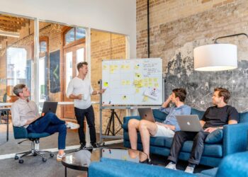 tiga pria duduk sambil menggunakan laptop dan menonton pria di samping papan tulis