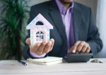 man holding model house at desk with calculator