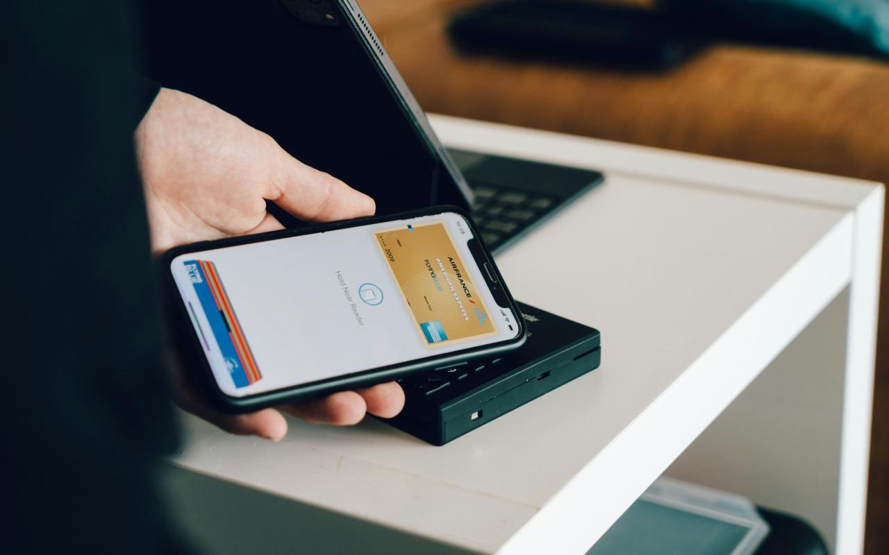 A person holding a smartphone over a card reader for contactless payment