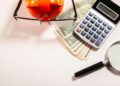 Calculator, magnifying glass, glasses, and money on white surface