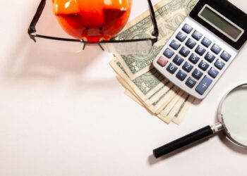 Calculator, magnifying glass, glasses, and money on white surface