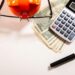 Calculator, magnifying glass, glasses, and money on white surface
