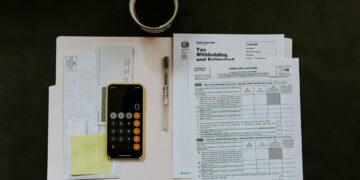 black Android smartphone near ballpoint pen, tax withholding certificate on top of white folder
